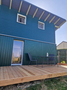 Ein grünes Holzhaus mit einer neuen Holzterrasse